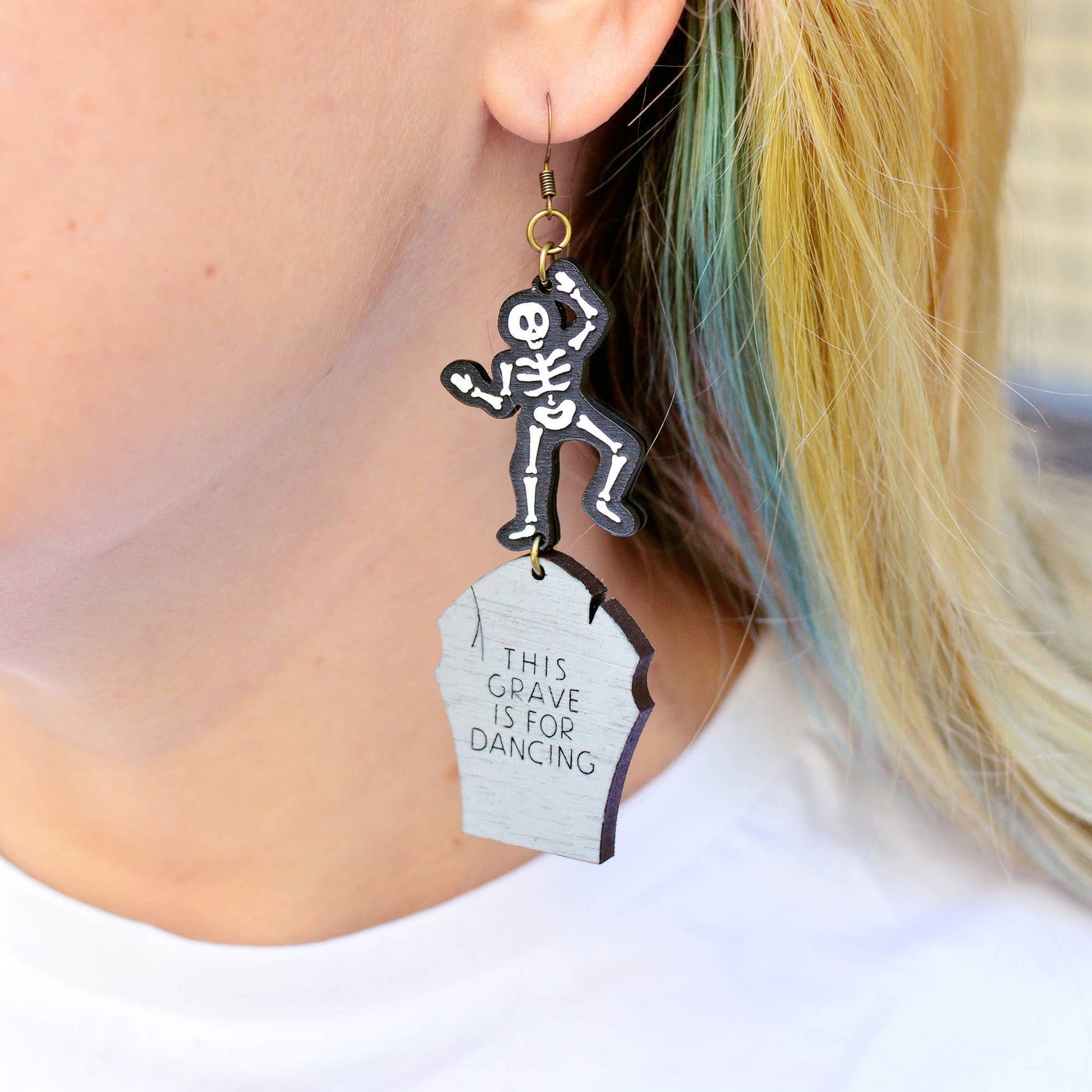 Statement earrings with a funny message, featuring a gravestone and skeleton for Halloween. This design depicts a skeleton dancing on it's own grave. The gravestone reads "this grave is for dancing".